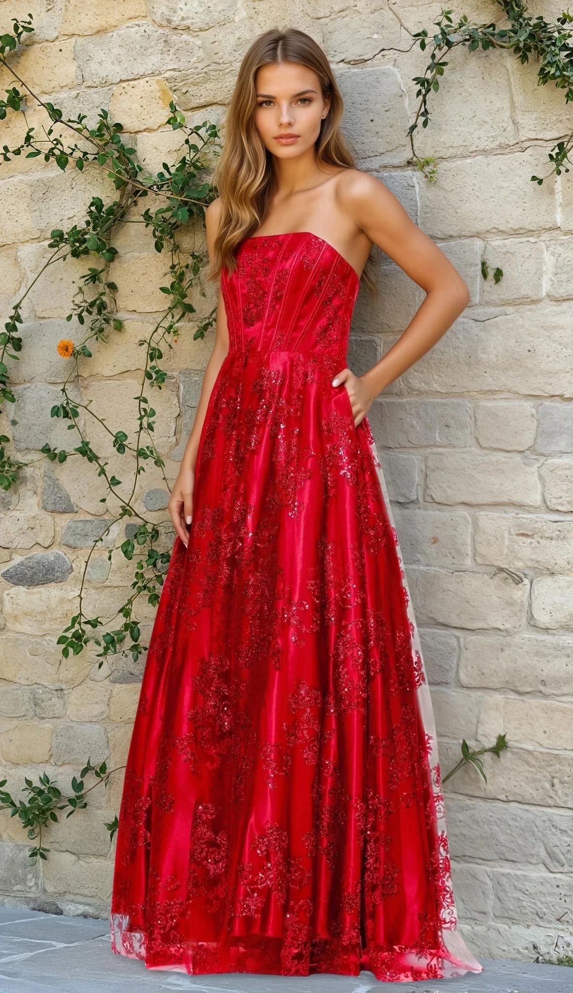 A woman stands before a vine-covered stone wall, wearing the Strapless Glitter Prom Dress Blondie Nites 4792BN in red.